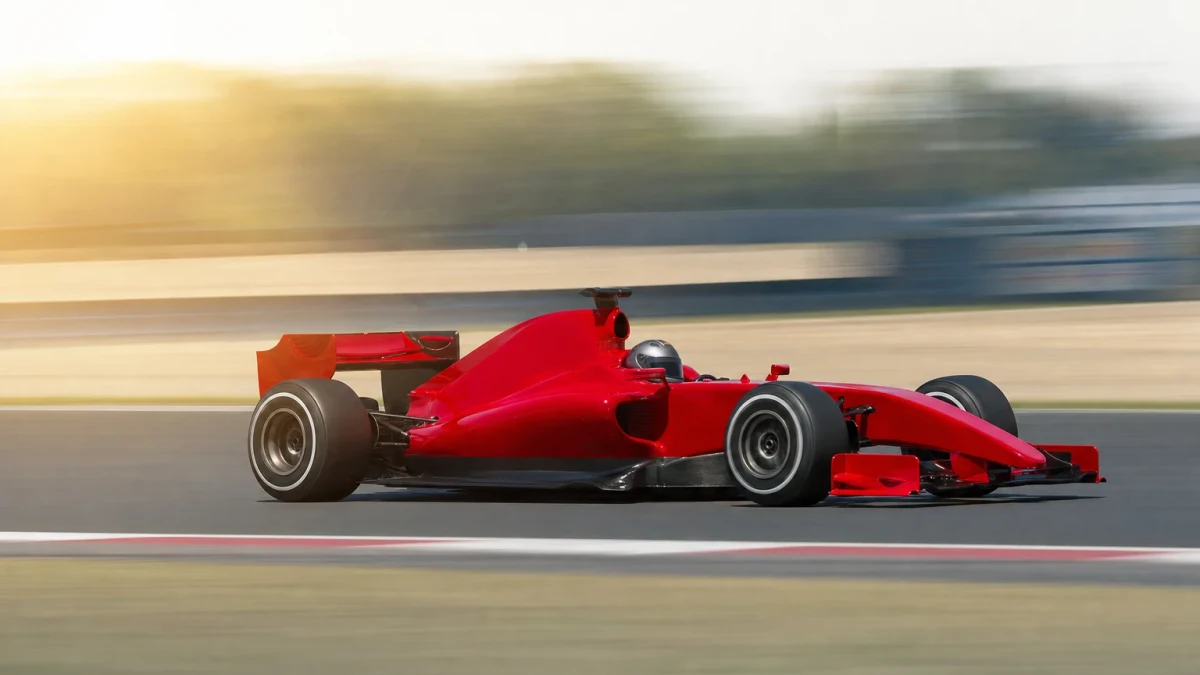 Klarröd formel 1-bil utan synliga sponsormärken på en solig racerbana.