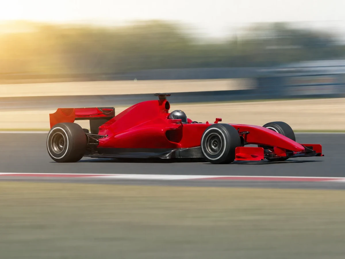 Klarröd formel 1-bil utan synliga sponsormärken på en solig racerbana.