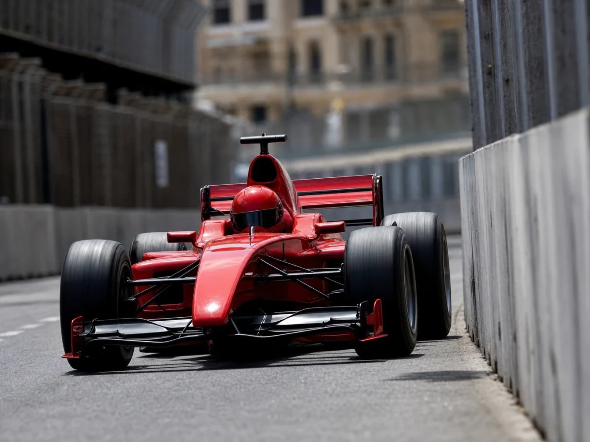 Röd formel 1-bil utan synliga sponsormärken på ett smalt gatlopp i starkt dagsljus.