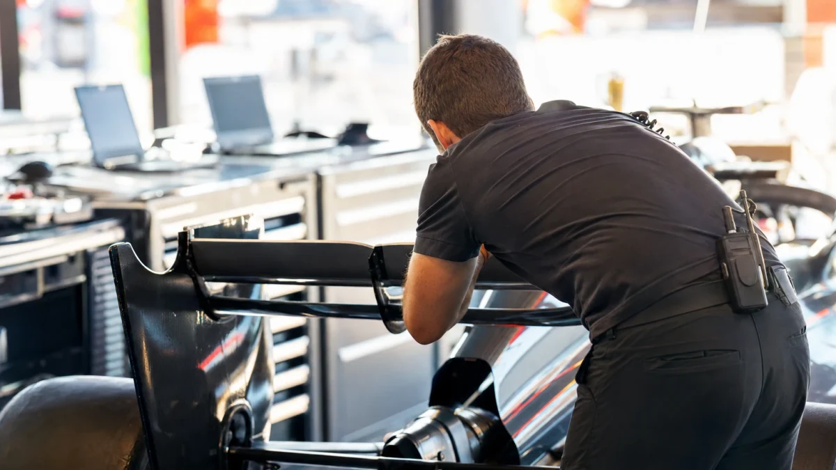 Ingenjör i teamklädsel lutad över en formel 1-bil i ett garage under en tävlingshelg.