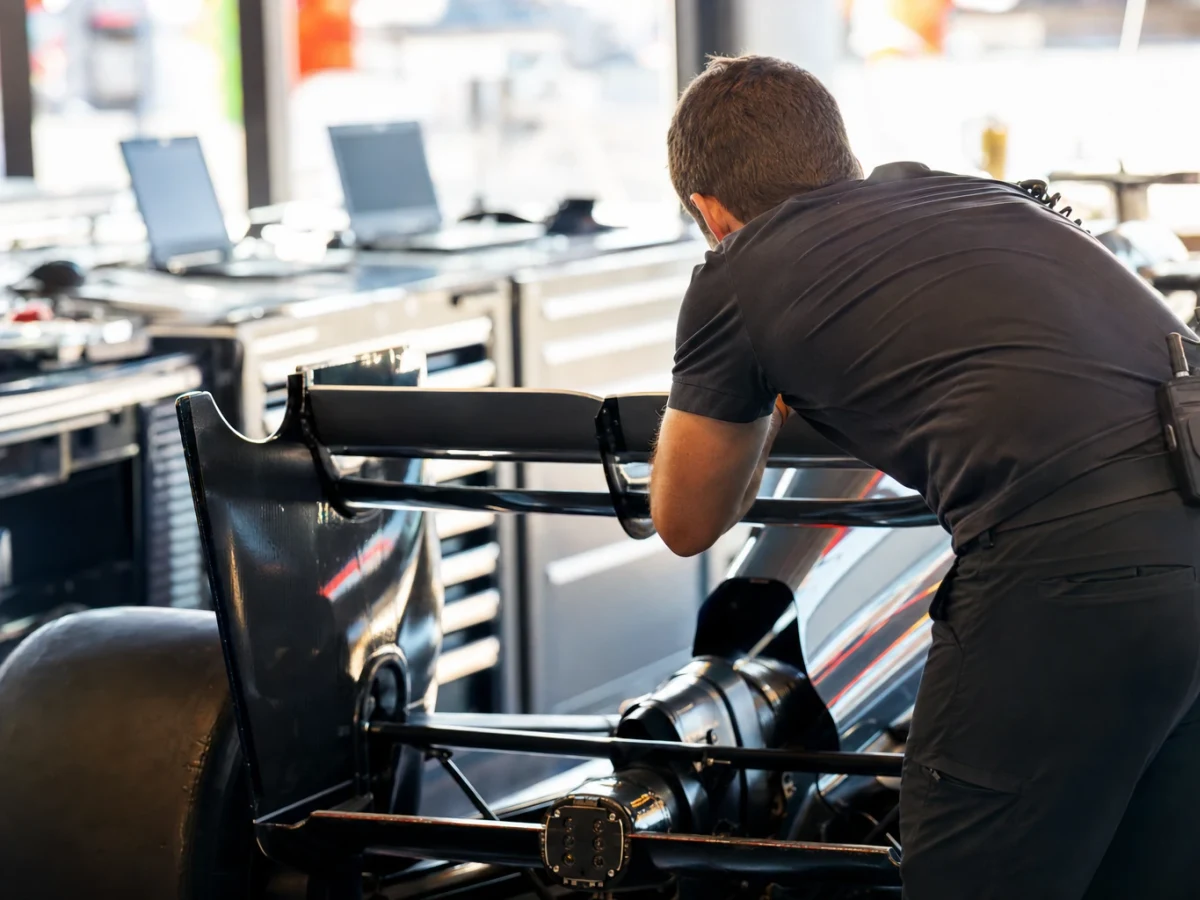 Ingenjör i teamklädsel lutad över en formel 1-bil i ett garage under en tävlingshelg.