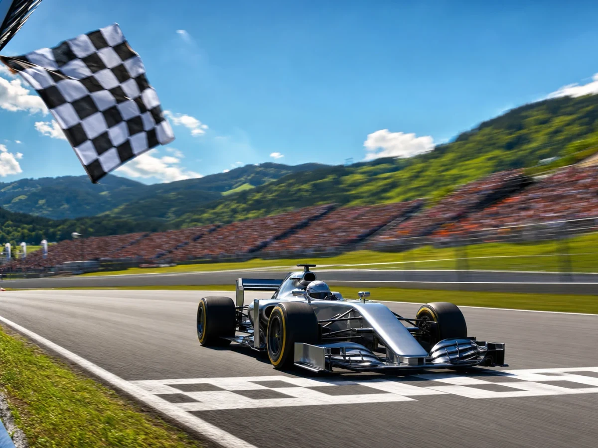 Silverfärgad formel 1-bil leder loppet över mållinjen på en bergig österrikisk racerbana i solljus.