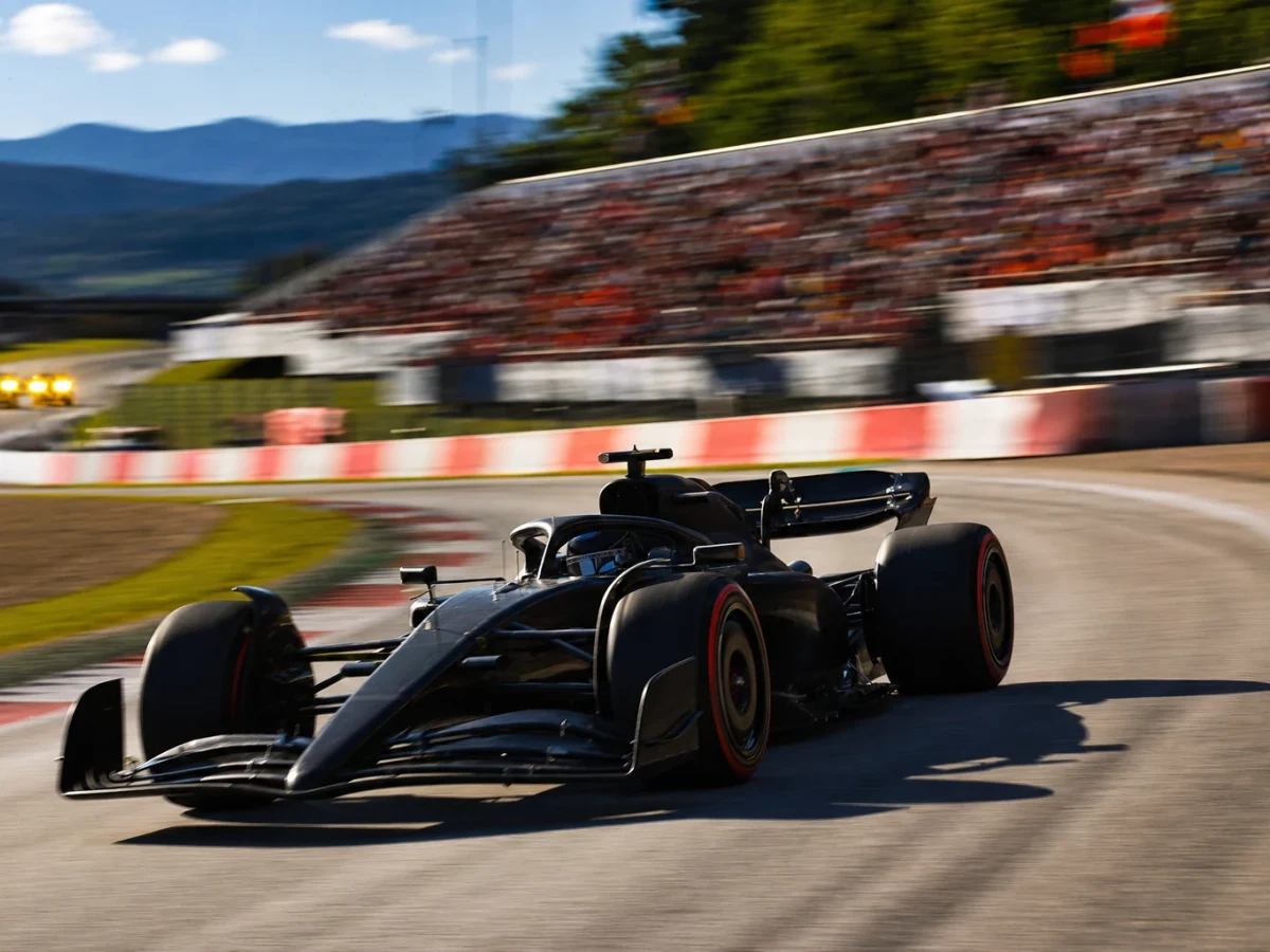 Formel 1-bil på Red Bull Ring i eftermiddagsljus med gula flaggljus tända vid en kurva i bakgrunden.