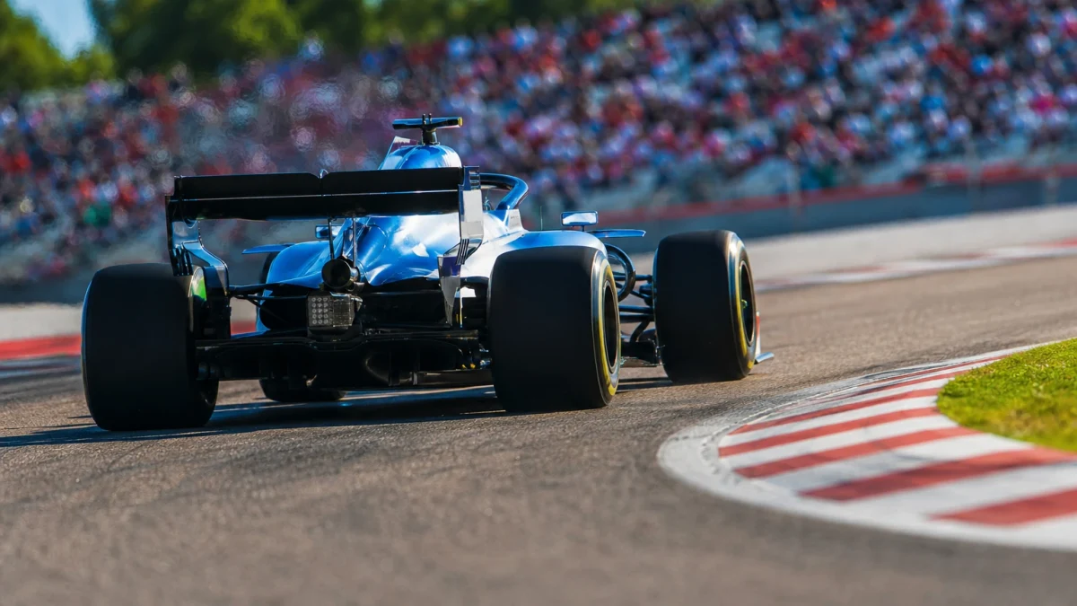 Formel 1-bil i blått och vitt genom en snabb kurva i skarpt kvällsljus, sedd bakifrån.