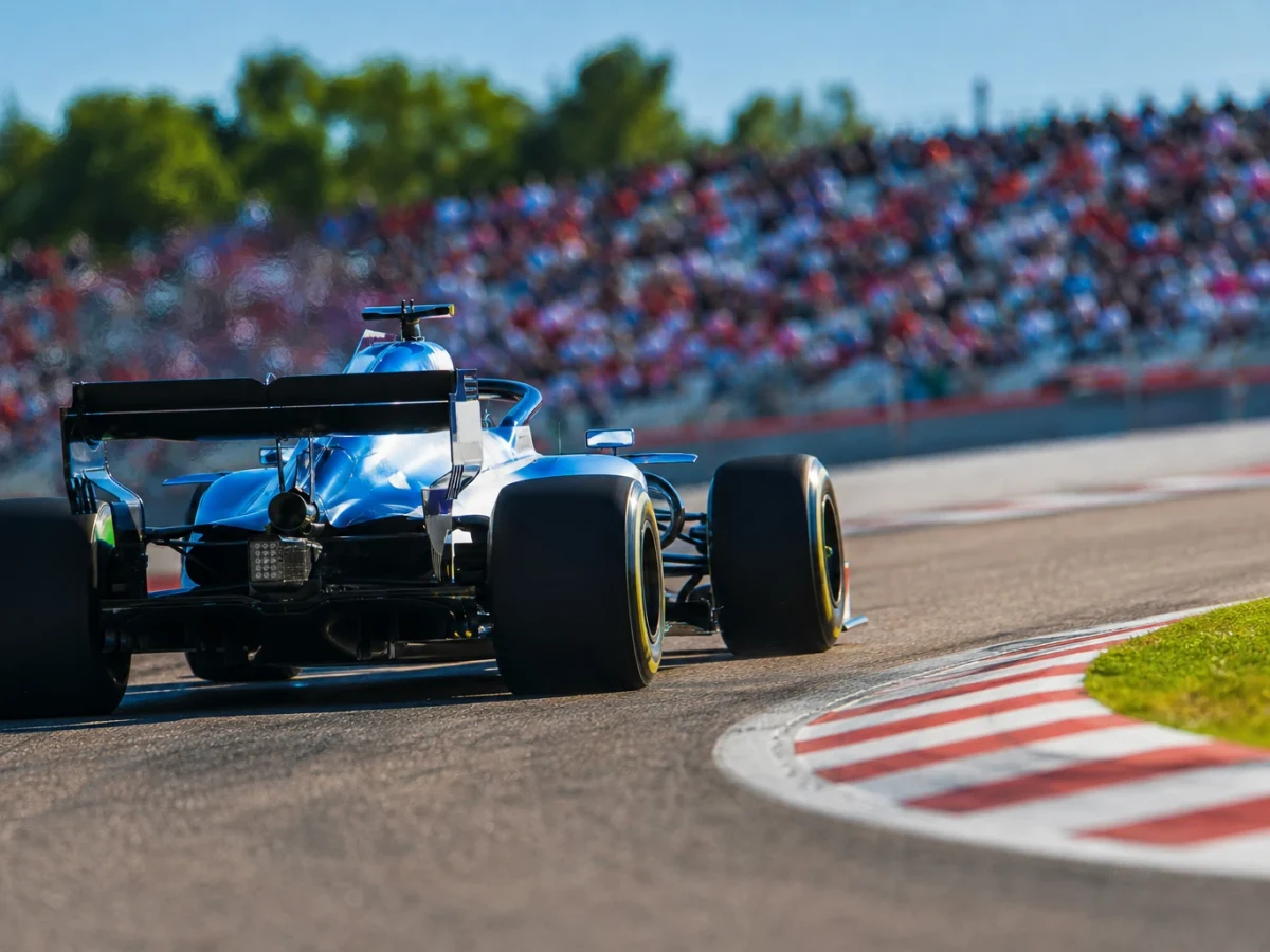 Formel 1-bil i blått och vitt genom en snabb kurva i skarpt kvällsljus, sedd bakifrån.
